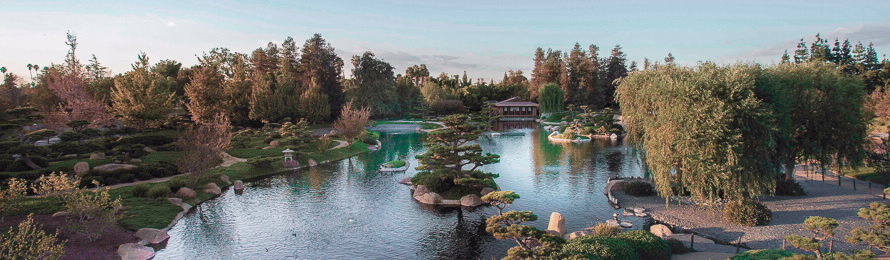 Panoramic view of a Japanese garden with a central pond, stone lanterns, and lush trees.