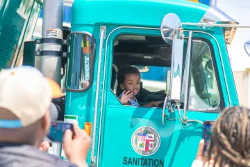 Parents stand close to take photos of their child sitting in one of LASAN's trash trucks at Earth Day LA